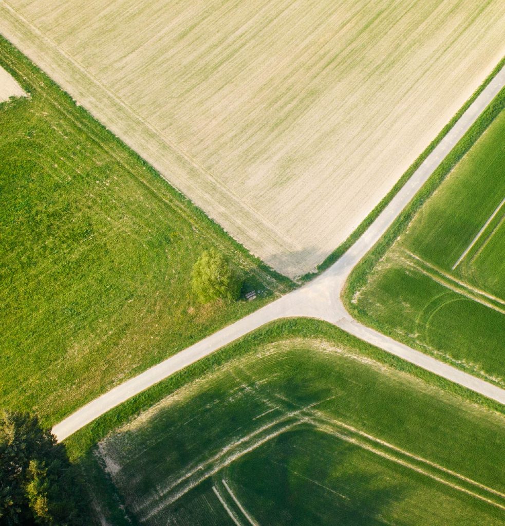 overhead perspective of a crossroad cutting through a vibrant green field