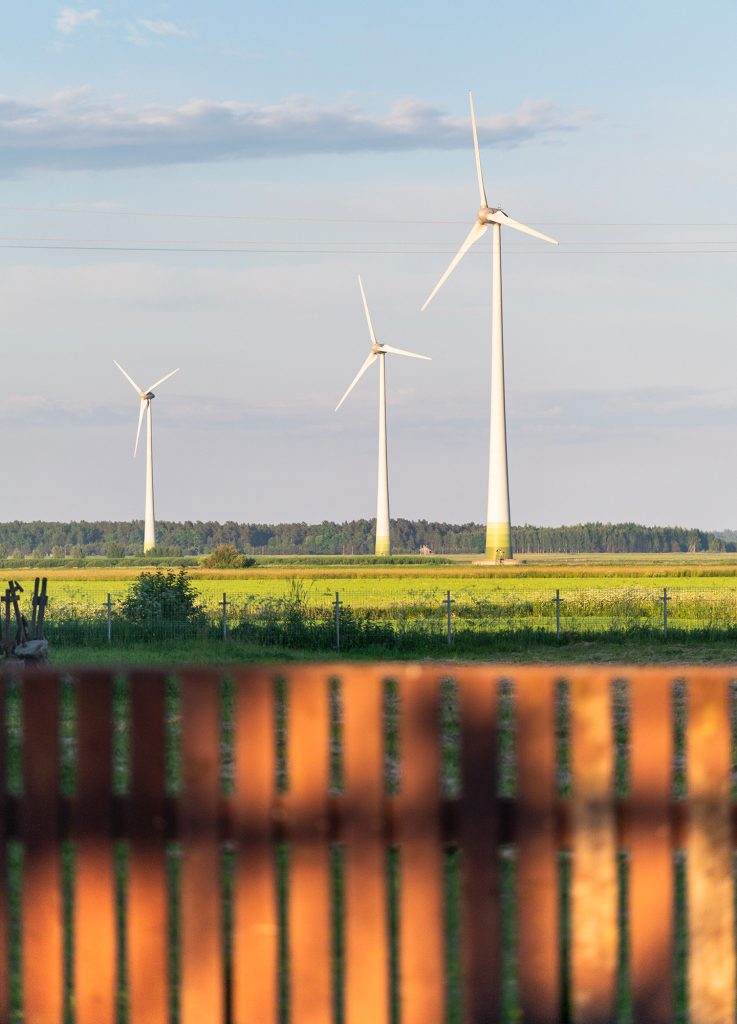 a side view of three wind turbines behind a wooden fence