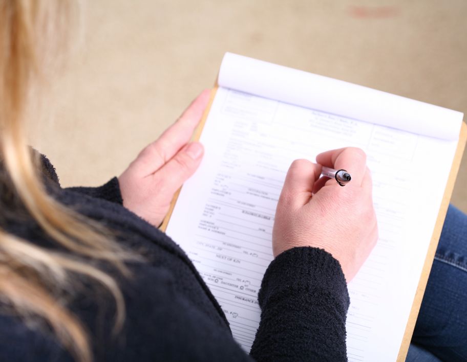 A woman filling up a form attached to a clipboard