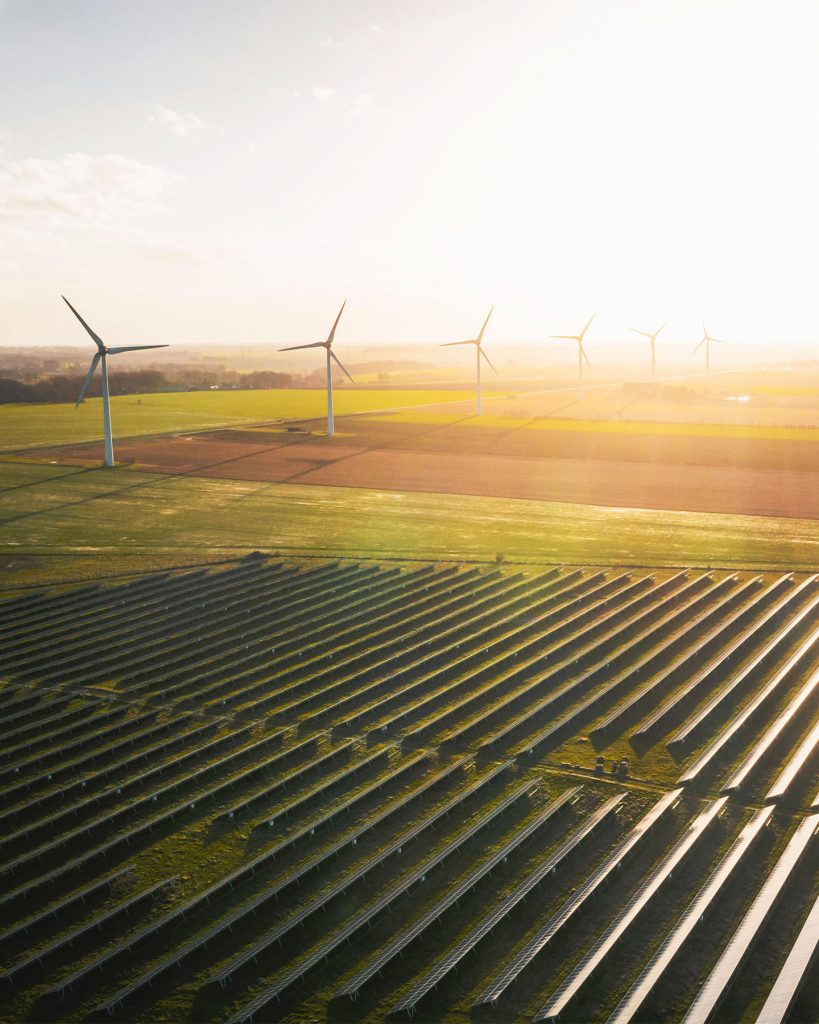 aerial view of wind turbines and rows of solar panels on a large field during sunset