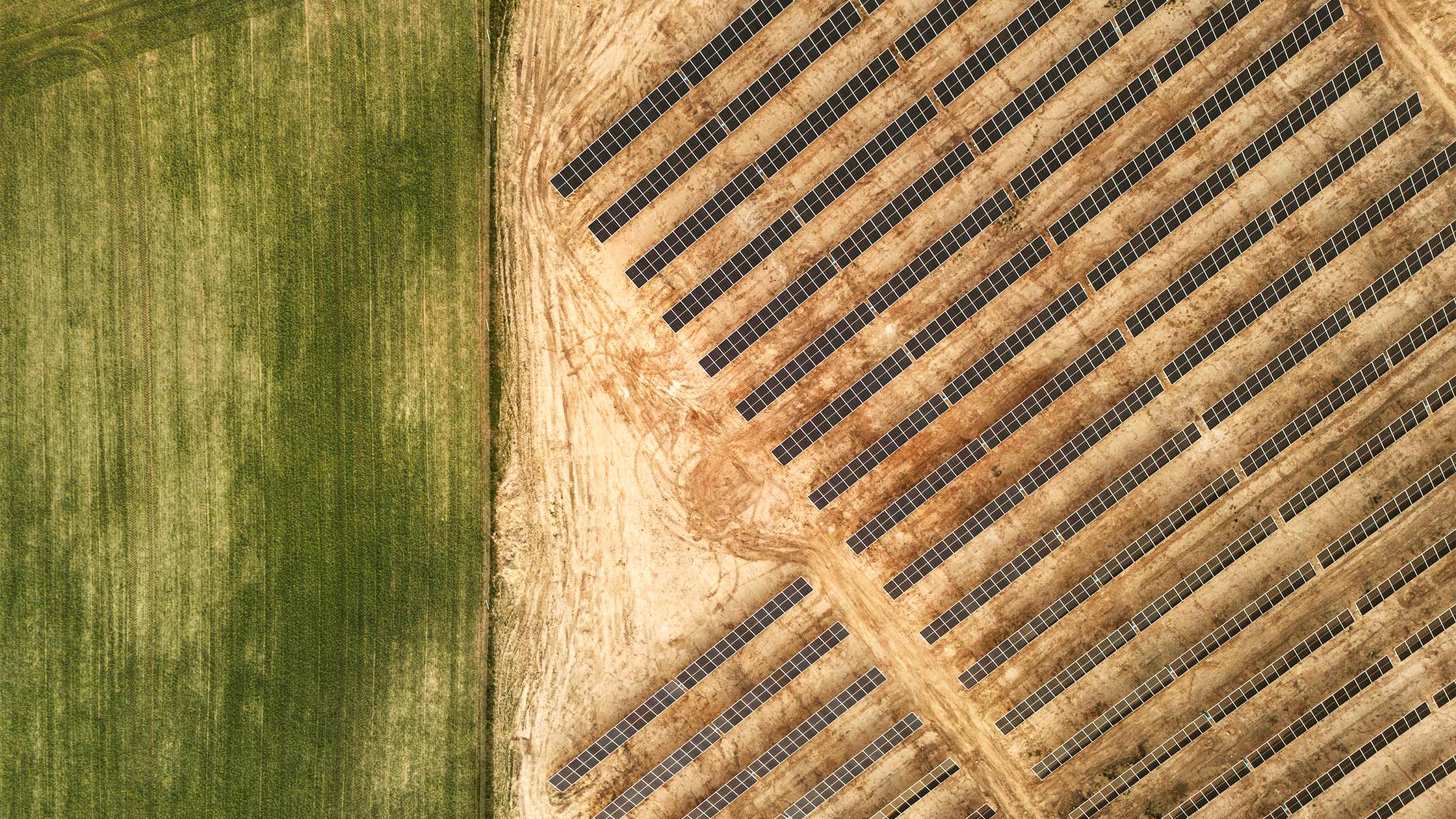 Aerial view of long rows of dark solar panels installed on dusty brown terrain